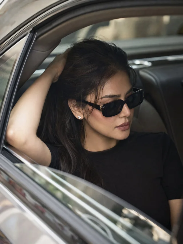 A luxury fashion editorial portrait of a woman in black sunglasses seated in the rear of a premium sedan, shot candidly through a lowered window.