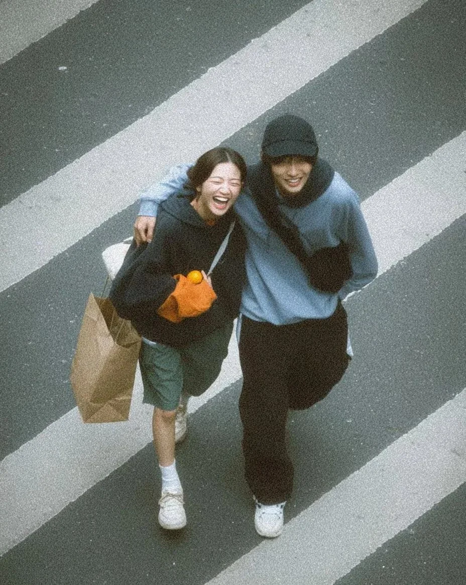 A documentary-style overhead street photo variation of a young couple walking playfully across a zebra crossing.